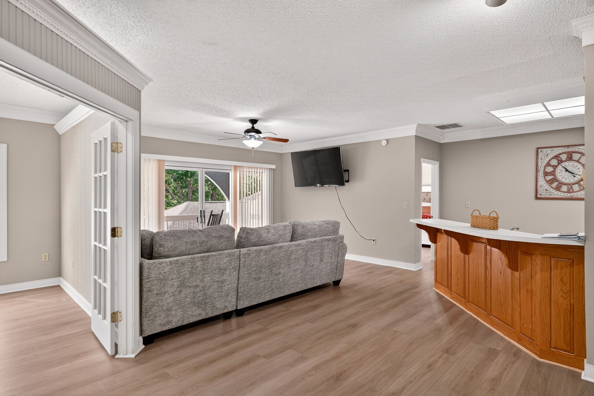 Living room with gray couch, TV, wood floor, and bar. French doors lead outside.