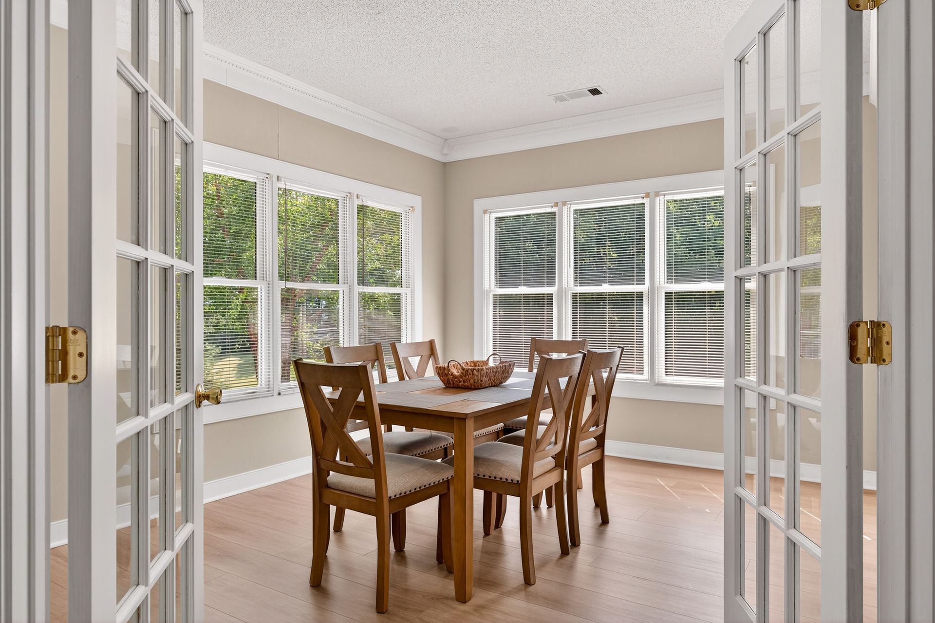 Dining room with a wooden table, chairs, and large windows; French doors open.