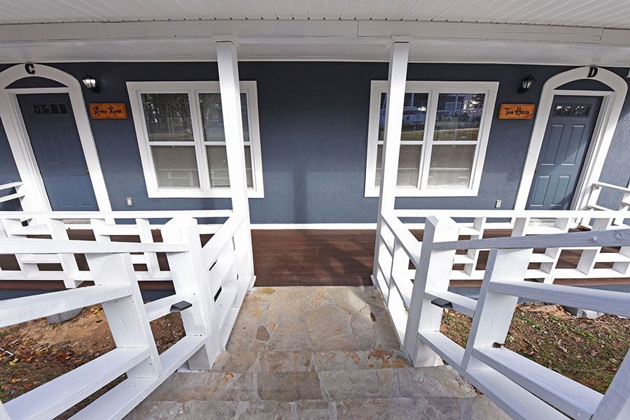 A white-railed staircase leads to a blue building with two doors and windows.