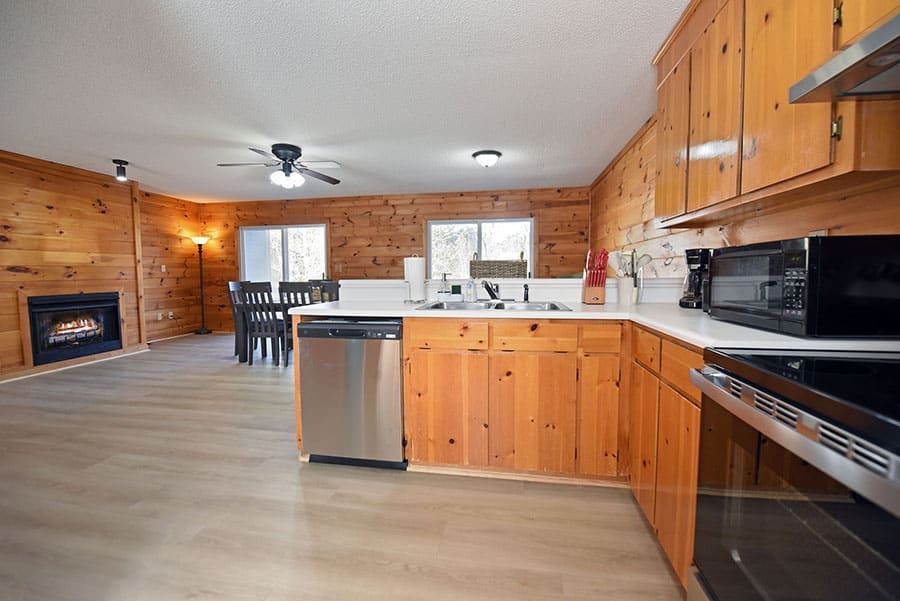 Kitchen with wood paneling, stainless steel appliances, and a view of a dining area with a fireplace.