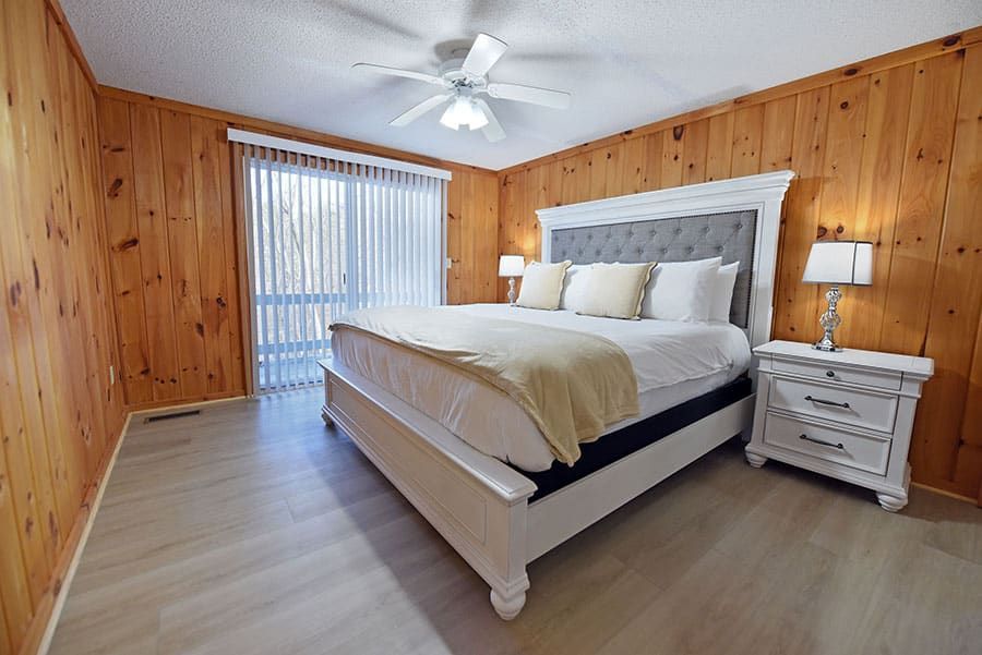 Bedroom with light wood walls, a large white bed, and a sliding glass door.