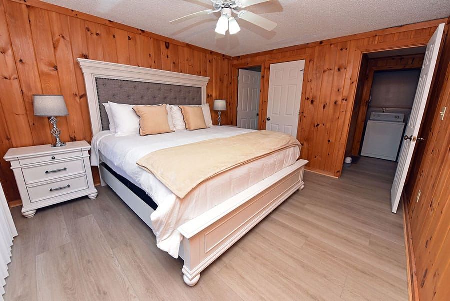 Bedroom with wood panel walls, a white bed, nightstand, and a doorway to a laundry area.