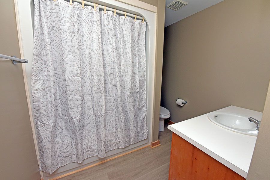 Bathroom with shower curtain, toilet, sink, and wooden vanity. Beige walls and light-colored flooring.