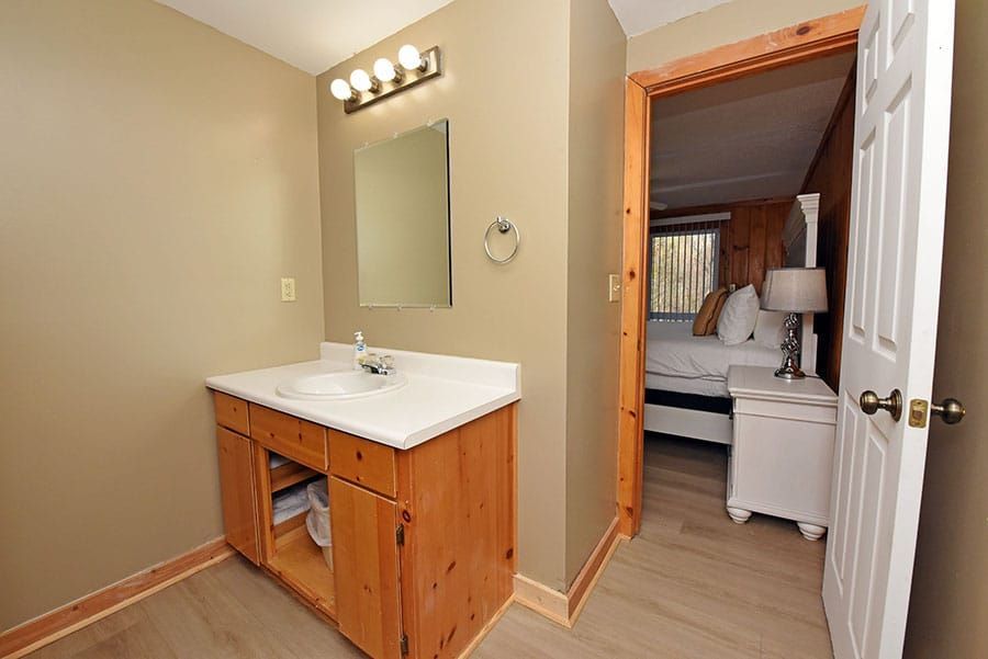 Bathroom with wooden vanity, sink, mirror, and doorway leading to bedroom.