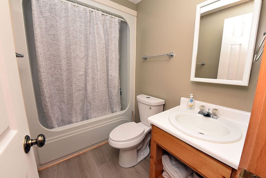 Small bathroom with a tub/shower, toilet, vanity, and mirror. Light gray walls and flooring.