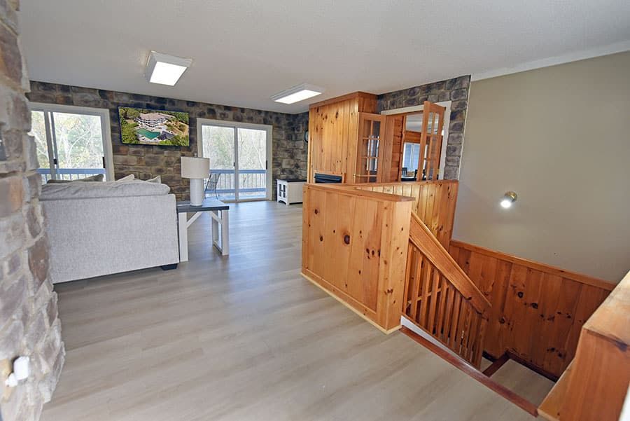 Living room with stone walls, light wood paneling, stairs, and a sofa near a sliding glass door.