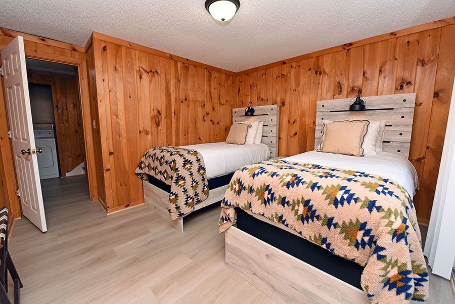 Two twin beds in a rustic bedroom with wood paneling, white bedding, and patterned blankets.