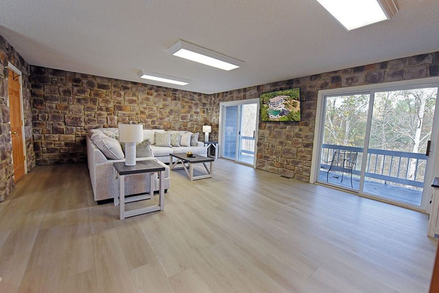 Living room with stone walls, light wood floors, a white sofa, and sliding doors to a balcony.