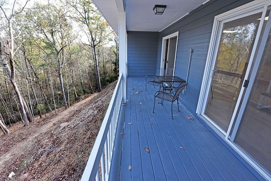 A deck with a small table and chair, overlooking a wooded hillside.