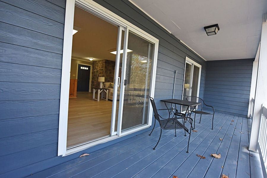 Blue-sided home porch with sliding glass door, table, chairs, and glimpse of interior living room.