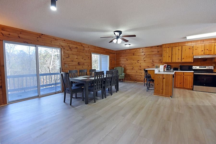 Spacious kitchen and dining area in a log cabin with a long table, stainless steel appliances, and large sliding doors.