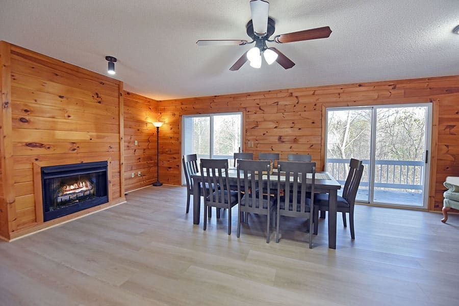 Dining area with wooden panel walls, fireplace, table, and a sliding door to a deck.