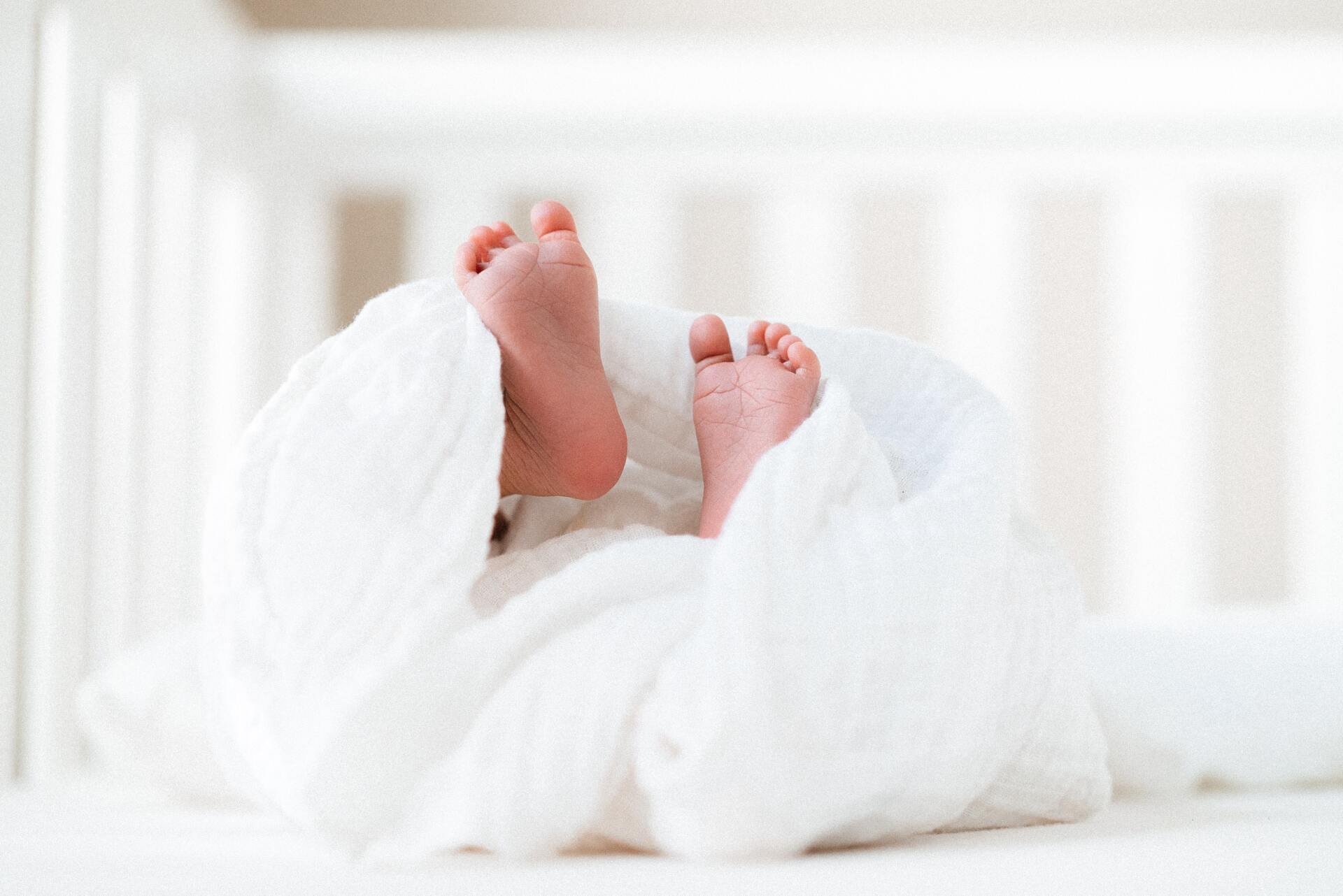 Little baby feet with ten tiny toes in a white crib with a linen blanket 