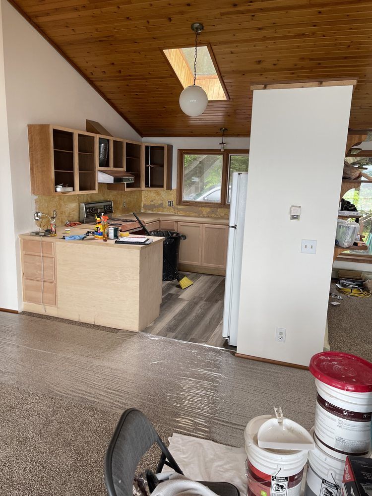 Small kitchen with wood ceiling, light cabinets, and a white partition in a rustic open-plan interior.