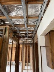 Interior construction site with exposed framing, foil insulation in ceiling, and unfinished doorway opening.