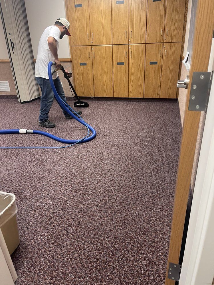 Worker vacuuming a carpeted office hallway beside wooden storage cabinets