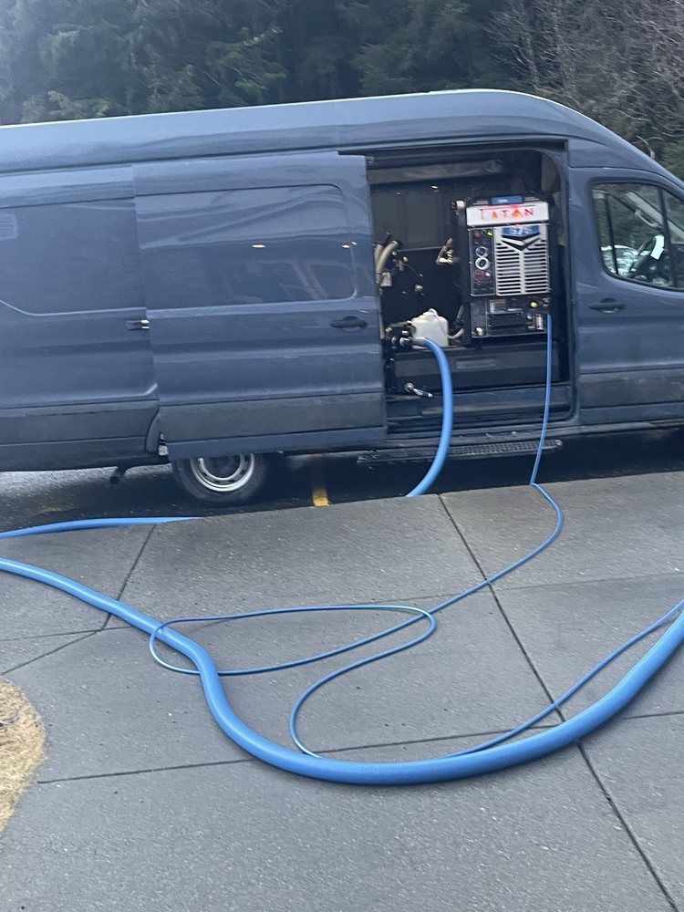 Blue van with side panel open, parked on a street, connected to equipment by blue hoses.