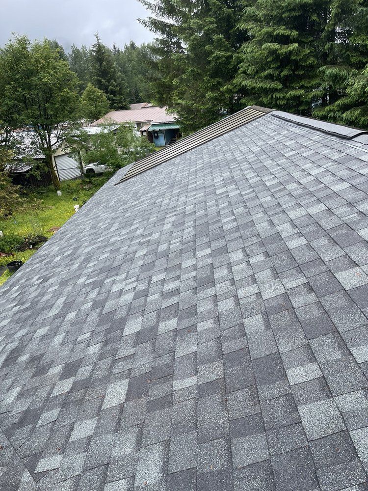 Gray shingled roof with trees and a house in the background