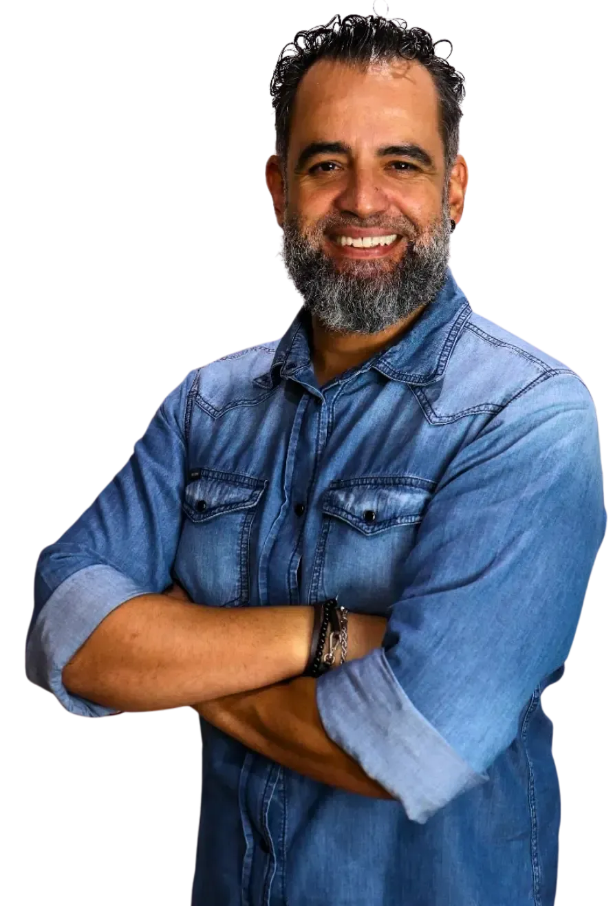 Um homem com barba está de pé com os braços cruzados e sorrindo.