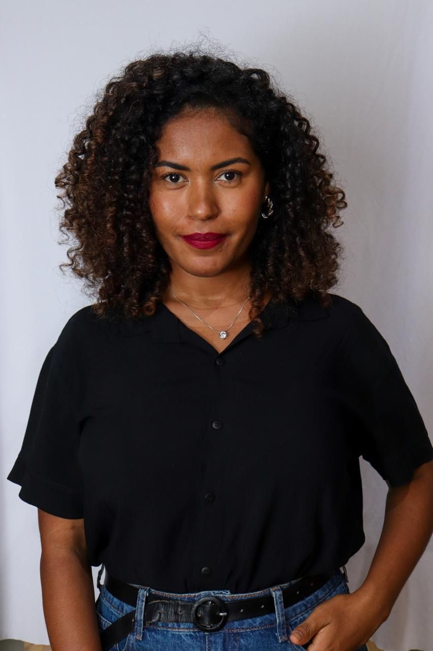 Uma mulher com cabelos cacheados está sorrindo para a câmera.