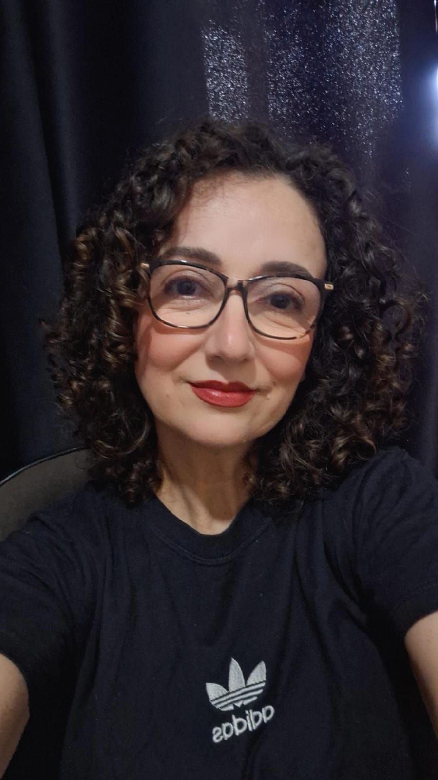 Um homem vestindo uma camisa preta e uma corrente de ouro sorri com os braços cruzados