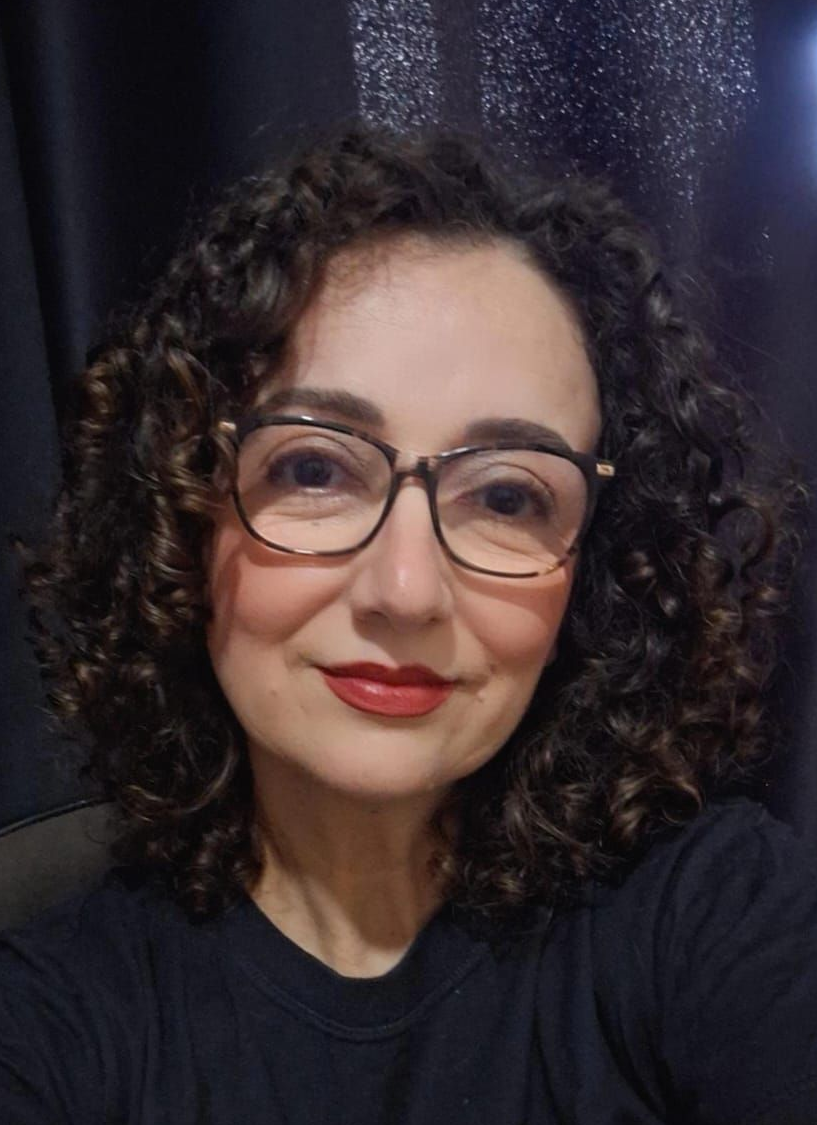 Um homem vestindo uma camisa preta e uma corrente de ouro sorri com os braços cruzados