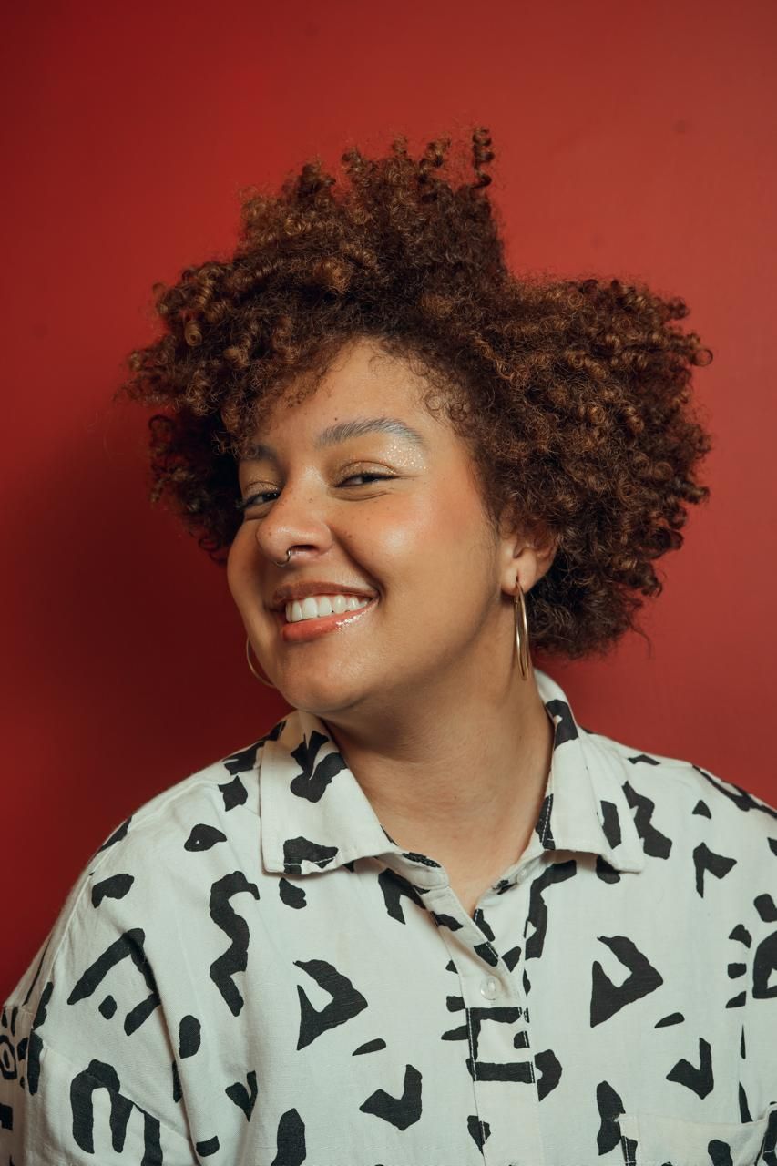 Um homem vestindo uma camisa preta e uma corrente de ouro sorri com os braços cruzados