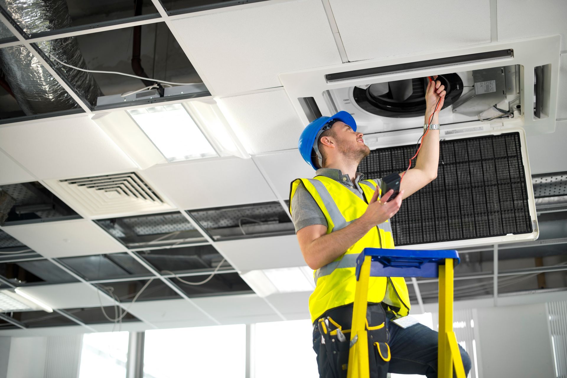 Man wearing safety gear plugs an AC vent with an electrical device.
