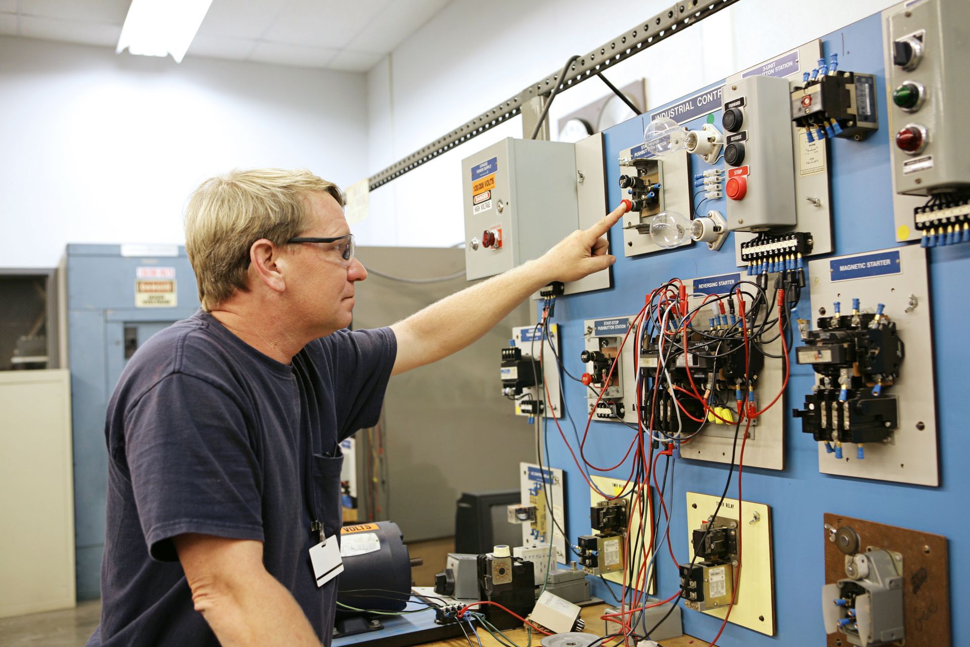 Technician adjusting electrical control panel with wiring and circuit components in industrial setting.