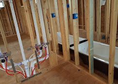Unfinished room frame with exposed plumbing pipes and two white bathtubs installed against the wall studs.