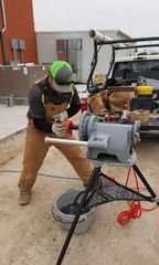 A worker in workwear uses a portable pipe threading machine on a tripod outdoors near a truck.