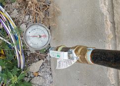 A pressure gauge attached to a pipe with a valve, situated on a concrete surface next to a bundle of multi-colored cables.