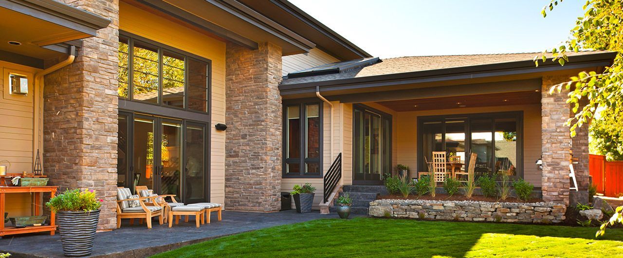 Exterior of a modern home with stone and stucco walls, a grassy lawn, and large windows.