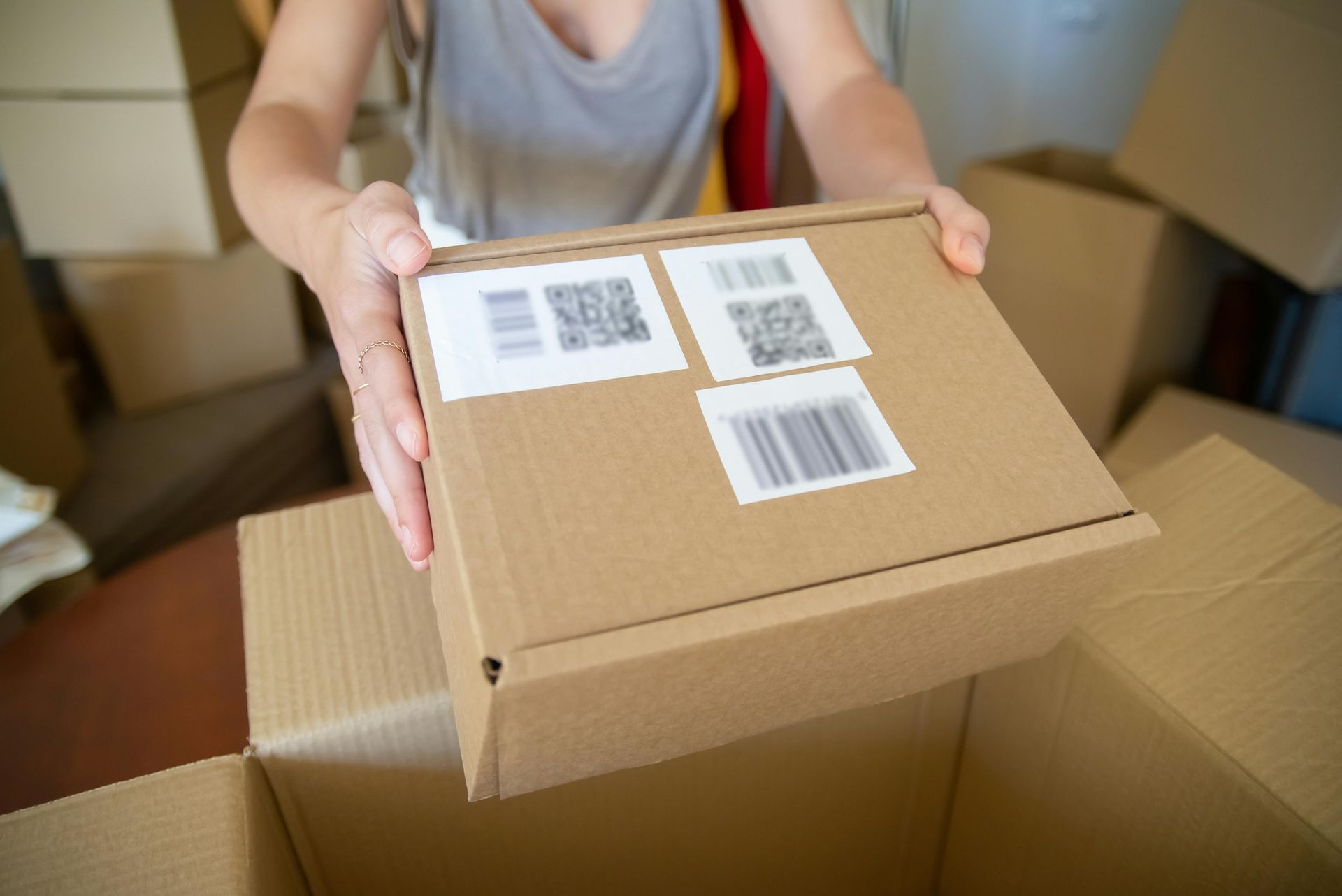 Person placing a cardboard box with shipping labels into another open box.