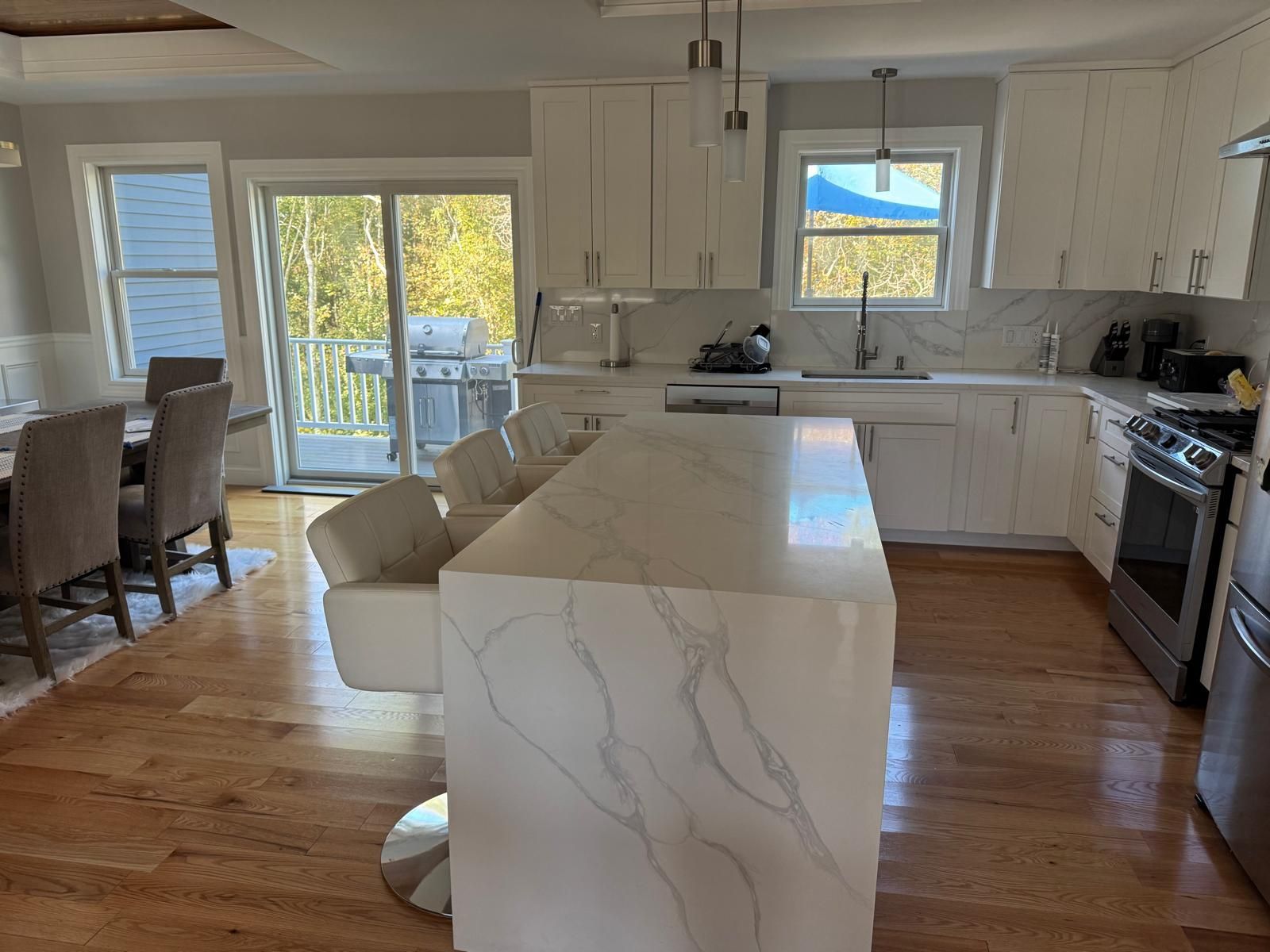 Modern kitchen with white cabinets, island, and stainless steel appliances; hardwood floors, and sliding glass door.