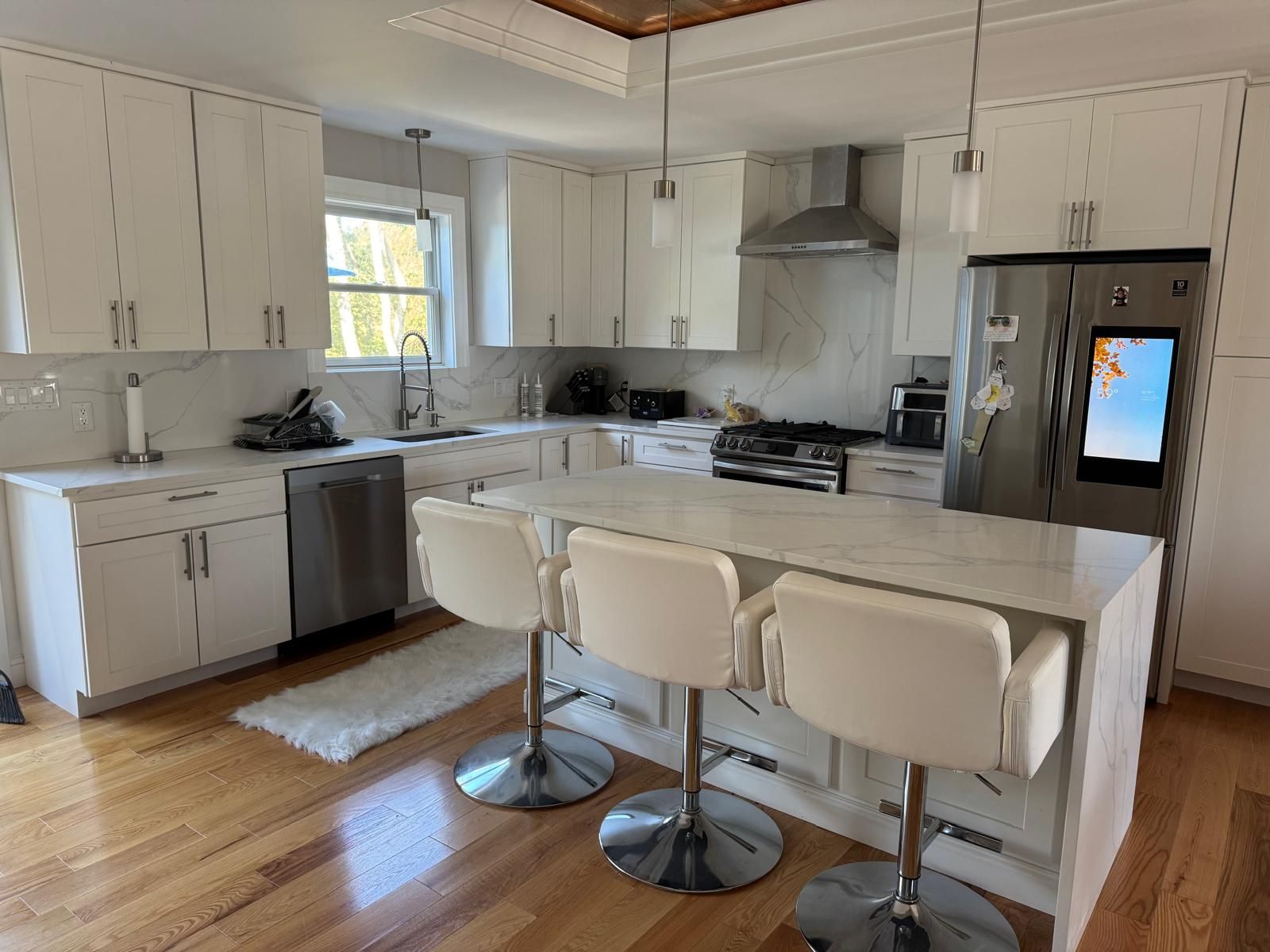 Modern white kitchen with island, stainless steel appliances, and hardwood floors.