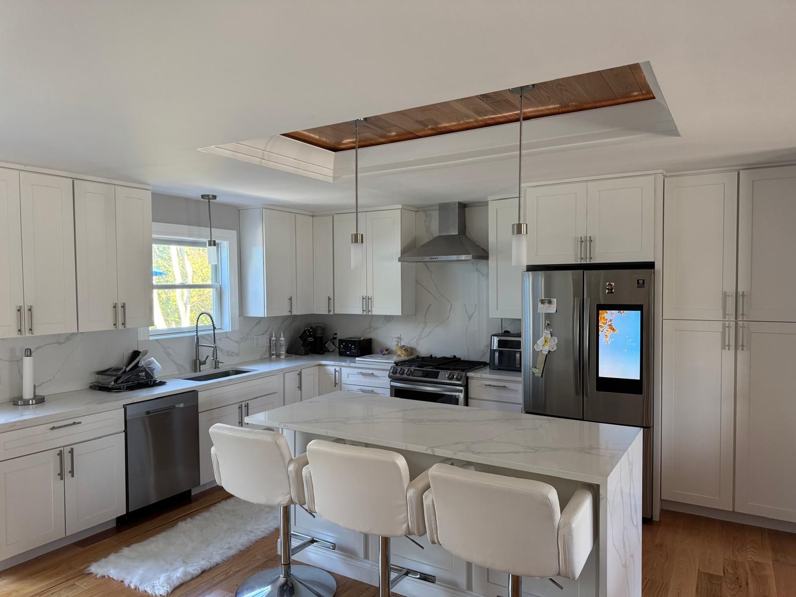 White kitchen with island and pendant lights; stainless steel appliances.