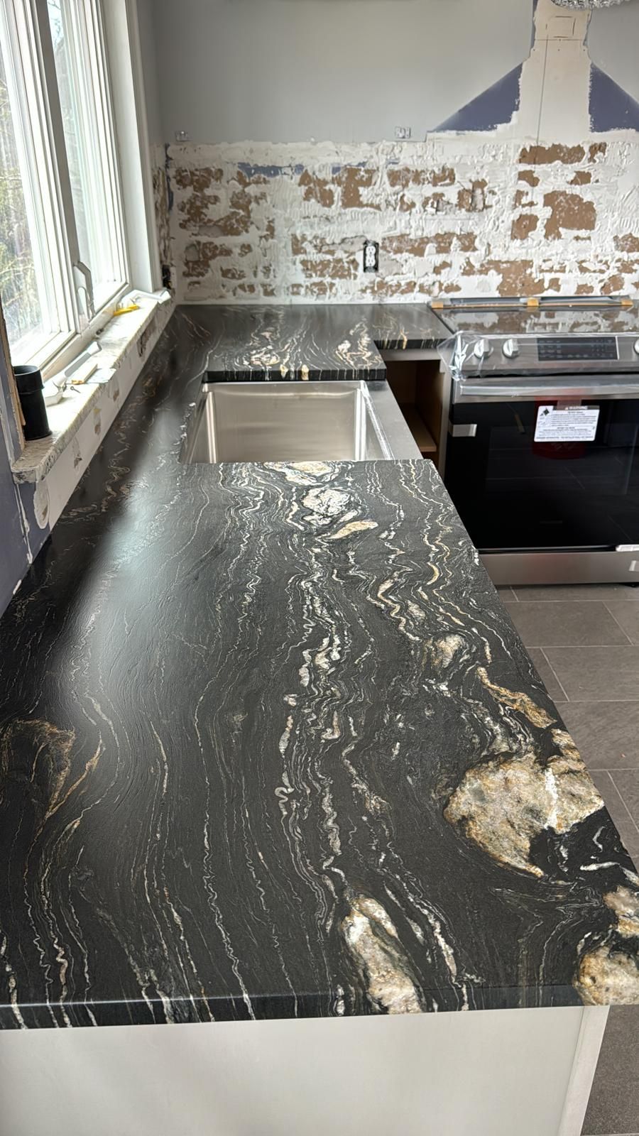 Black granite countertop with gold and white swirls, stainless steel sink, and stove.