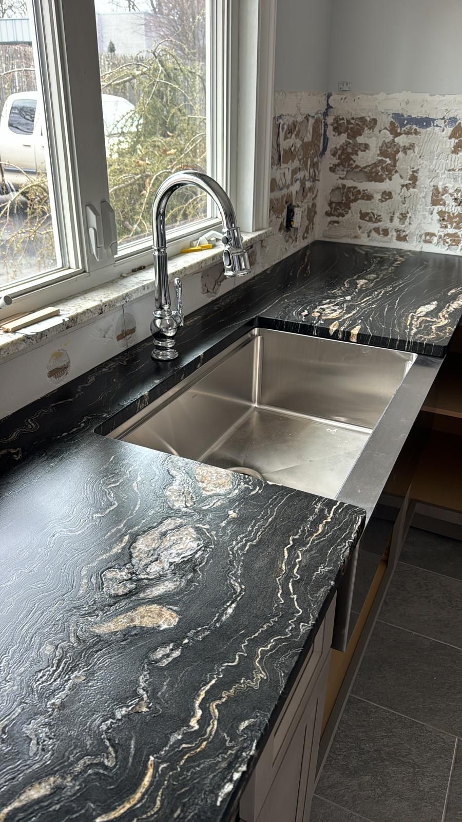 Black granite countertop with stainless steel sink and chrome faucet next to a window.