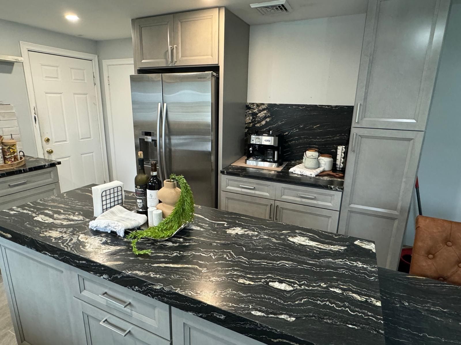 Kitchen with gray cabinets, stainless steel refrigerator, and black granite countertops.