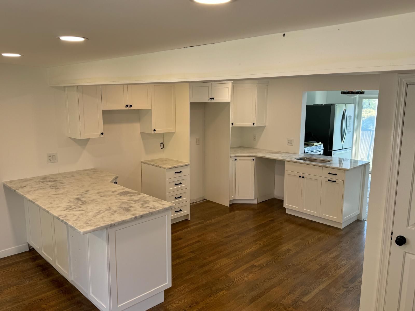 White kitchen with island, cabinets, and granite countertops. Wooden floor.