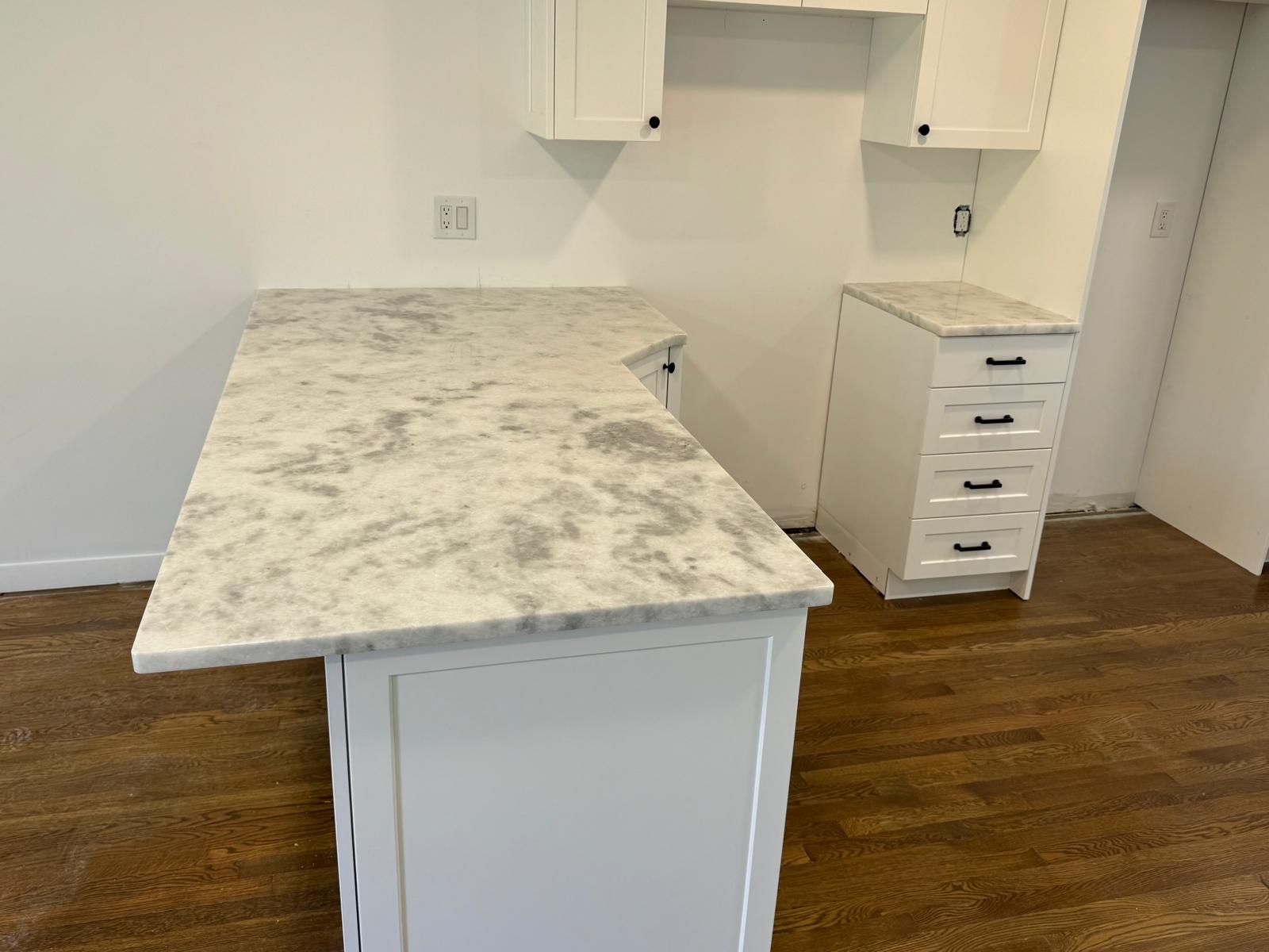 White kitchen island with marble countertop; cabinets, and drawers in a room with wood floors.