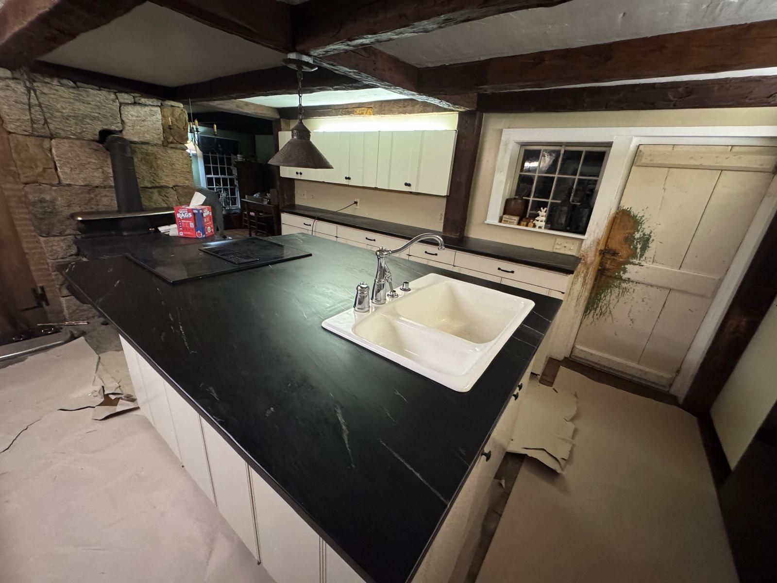 Kitchen with black countertop, white cabinets, sink, and window with wooden door.