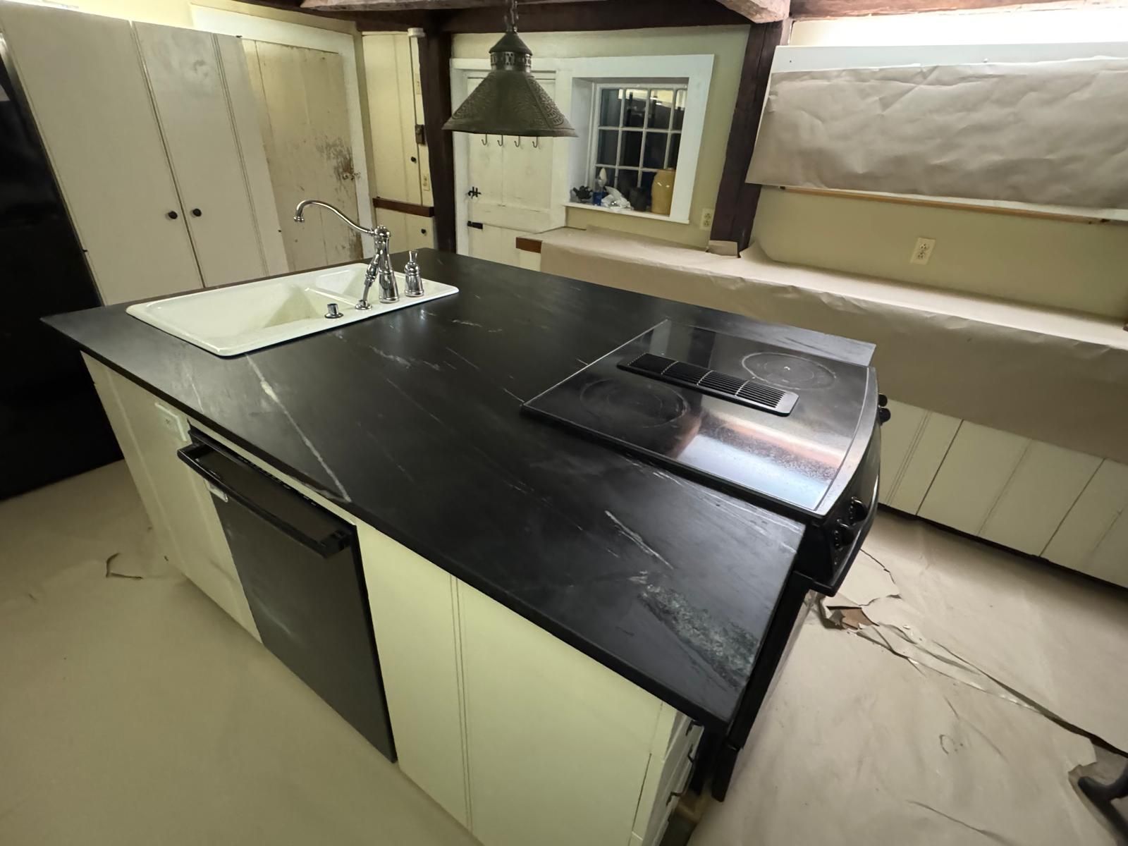 Kitchen island with black countertop, white cabinets, and built-in stovetop and sink.