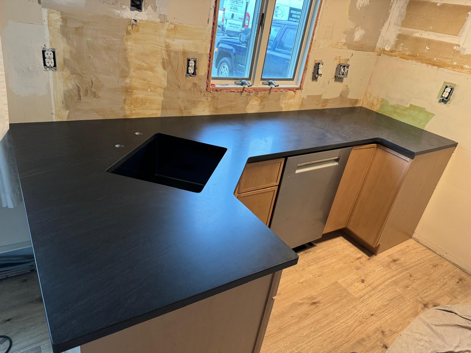 Black countertop installed in a kitchen with a sink, dishwasher, and cabinets.