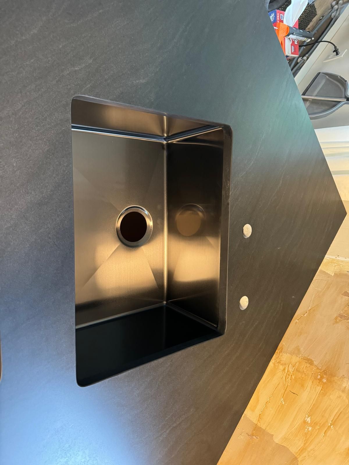 Stainless steel kitchen sink installed in black countertop.