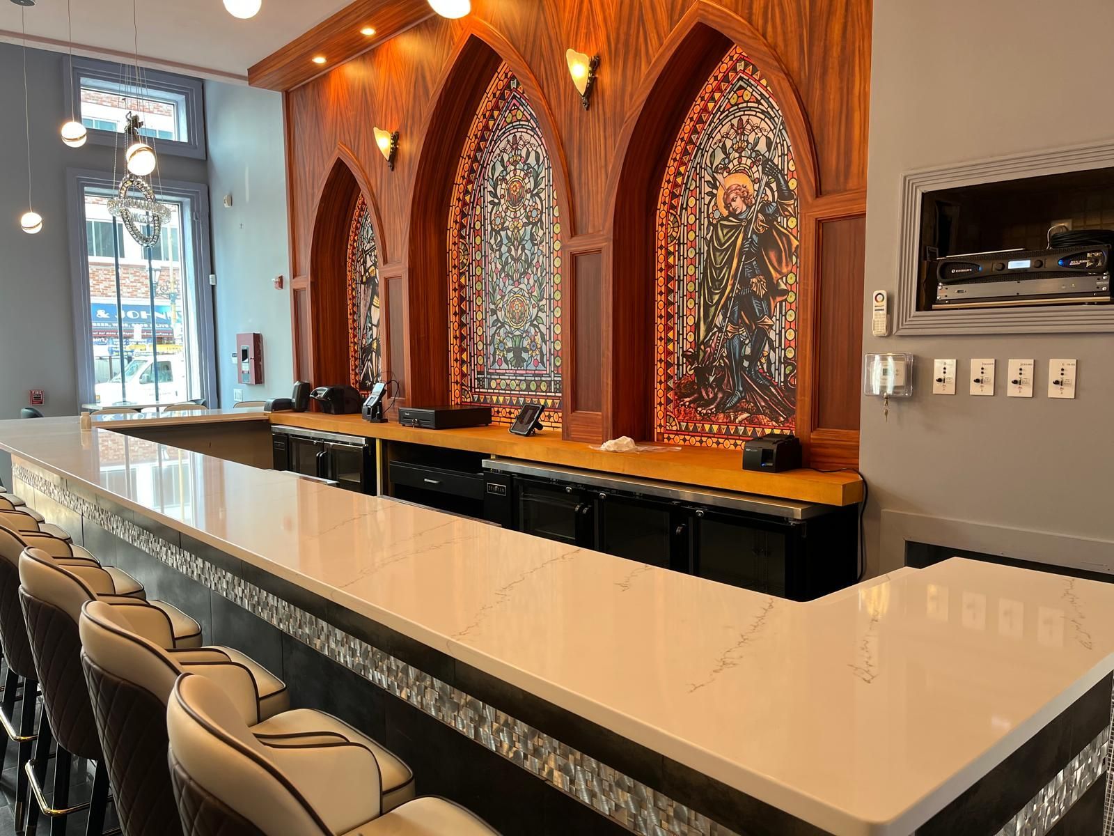 Bar with white countertop, dark chairs, and stained glass windows.