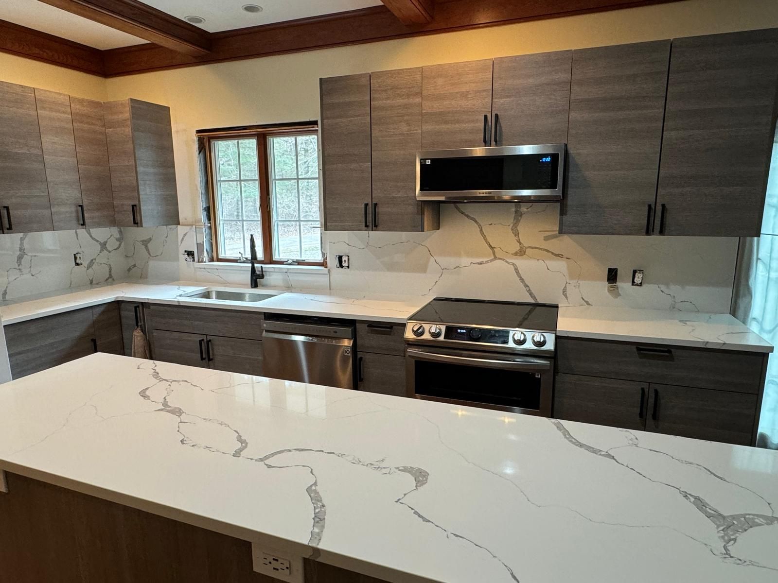 Modern kitchen with gray cabinets, white countertops, stainless steel appliances, and a large island.