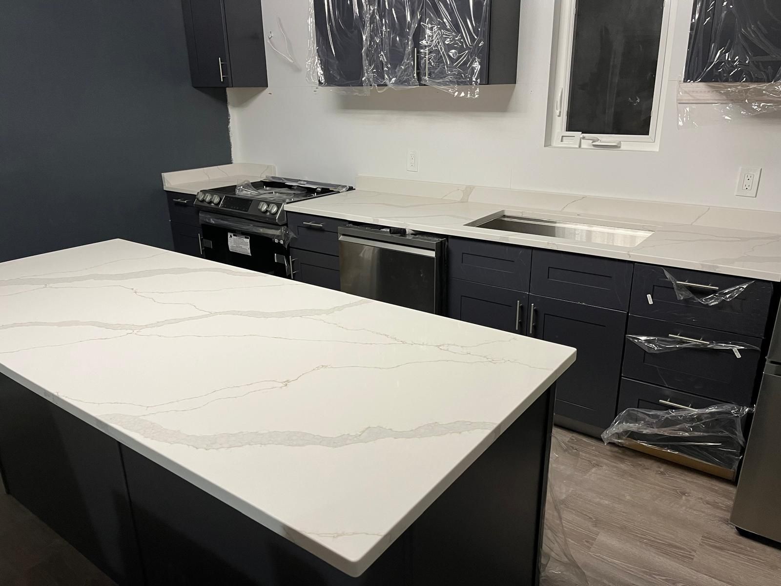 Modern kitchen with dark blue cabinets, white countertops, and stainless steel appliances.