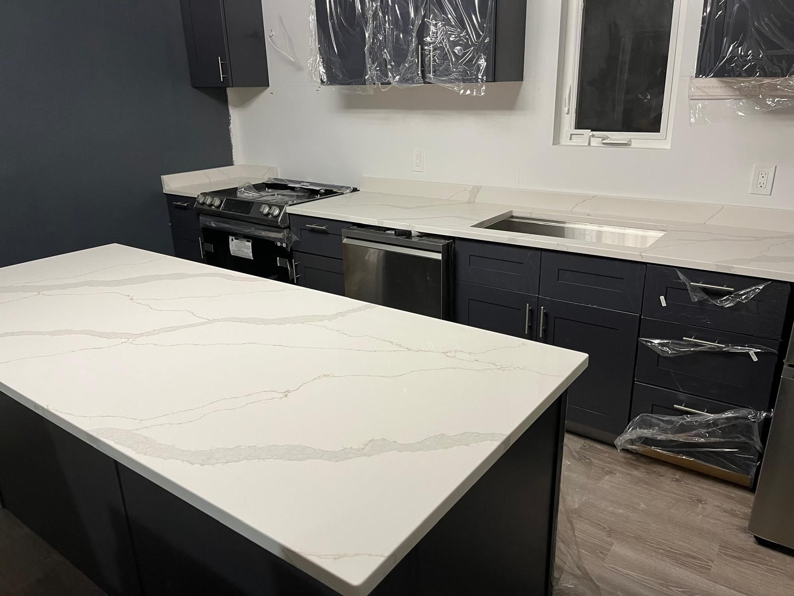 Modern kitchen with dark cabinets, white countertops, and stainless steel appliances.